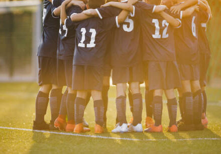 Group of children huddling with coach. Summer sunset at the stadium in the background. Youth soccer football team group photo. Happy boys soccer players kicking tournament. School boys in blue jerseys